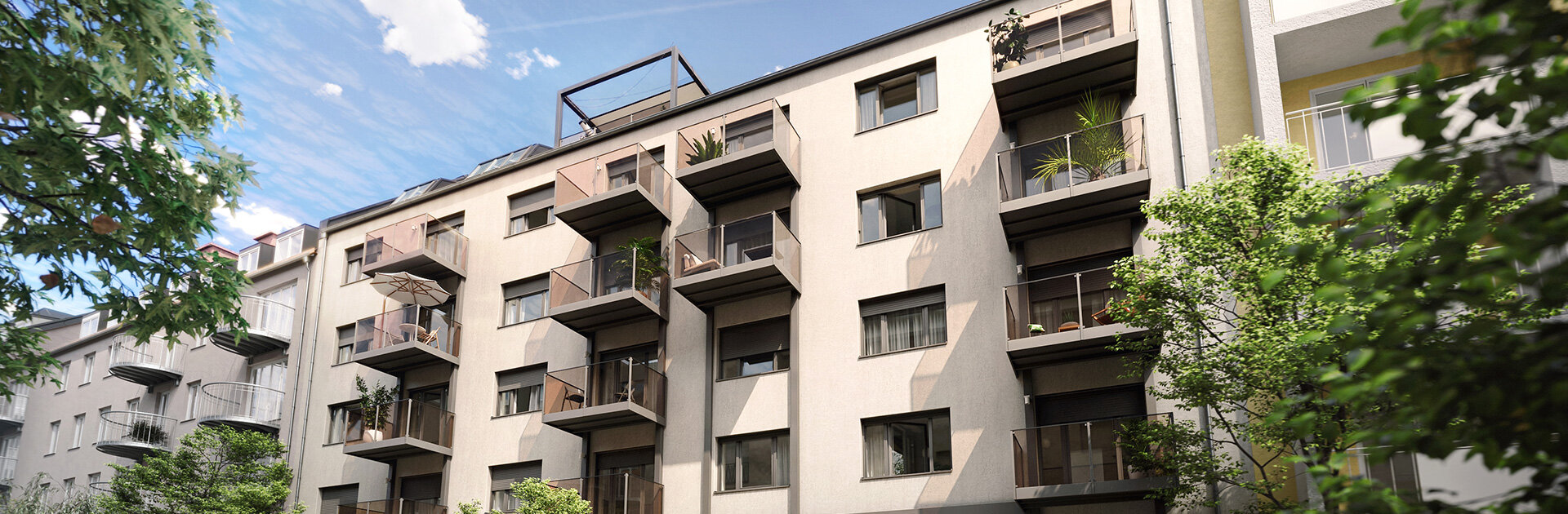 Ein modernes, mehrstöckiges Wohnhaus mit beige-grauer Fassade und dunklen Glasbalkonen. Links und rechts sind Bäume und Teile weiterer Gebäude sichtbar.