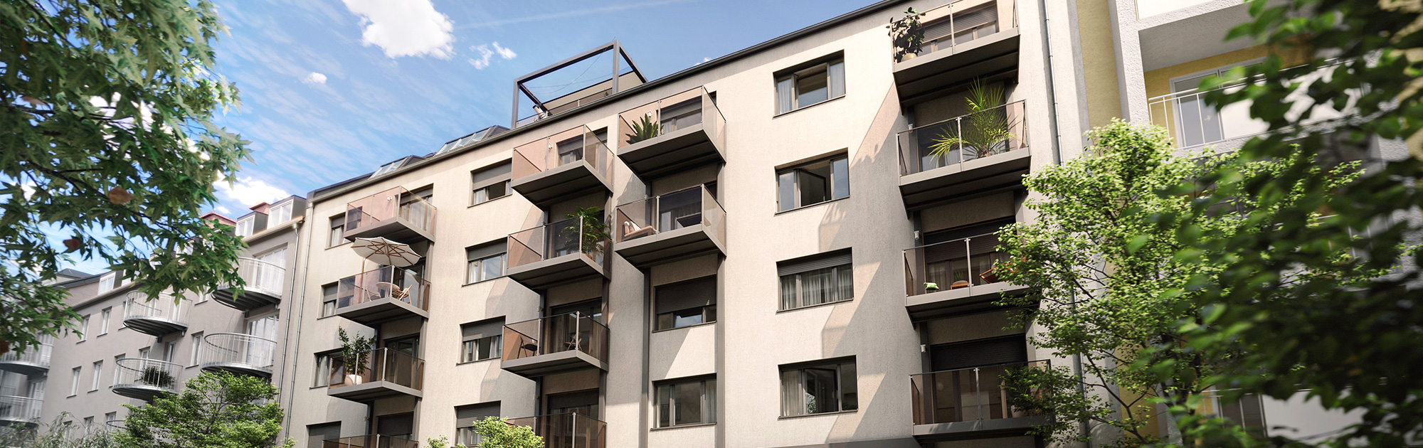 Ein modernes, mehrstöckiges Wohnhaus mit beige-grauer Fassade und dunklen Glasbalkonen. Links und rechts sind Bäume und Teile weiterer Gebäude sichtbar.