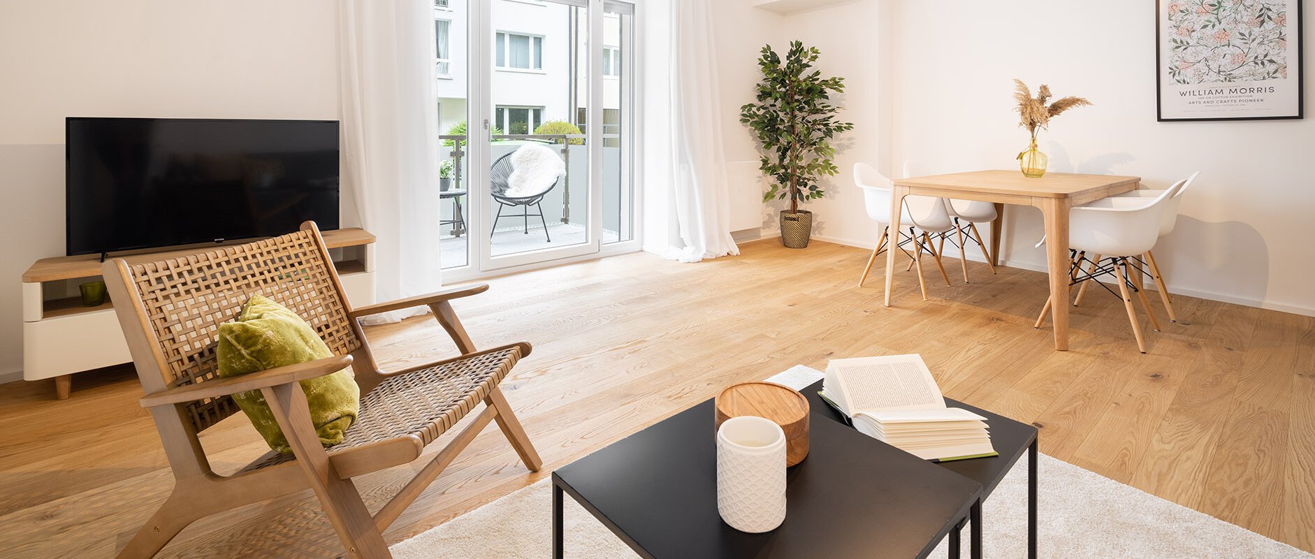Helles freundliches Wohnzimmer mit Blick auf Fernseher, Esstisch und Balkon