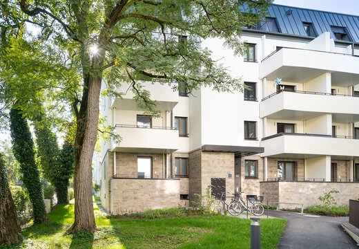 Außenansicht modernes Wohngebäude mit weißer Fassade, Erdgeschoss mit Steinvertäfelung und geräumigen Balkonen auf jeder Etage