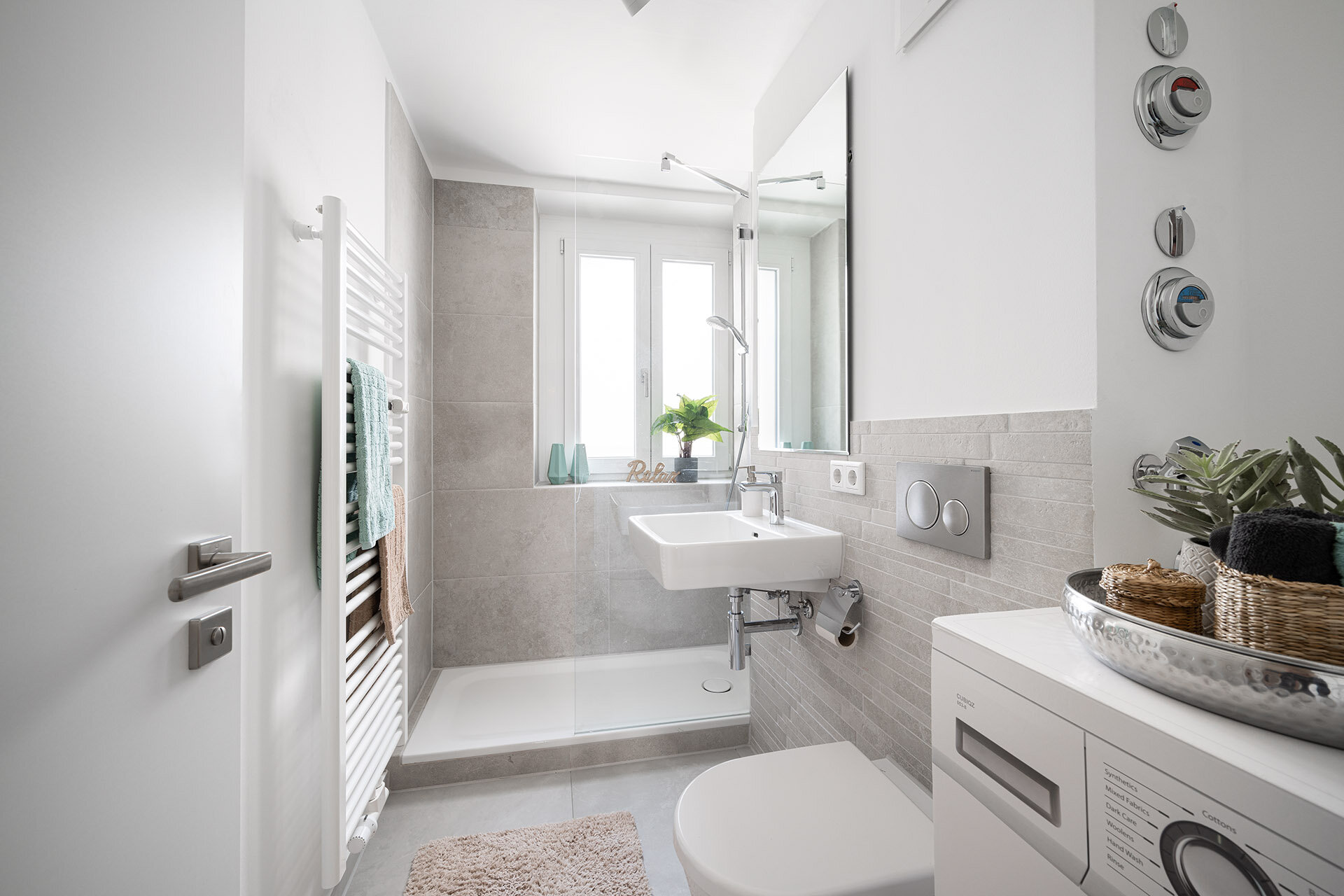 Helles lichtdurchflutetes Badezimmer mit Duschkabine, Waschbecken, Toilette und Waschmaschine, sowie Handtuchwärmer