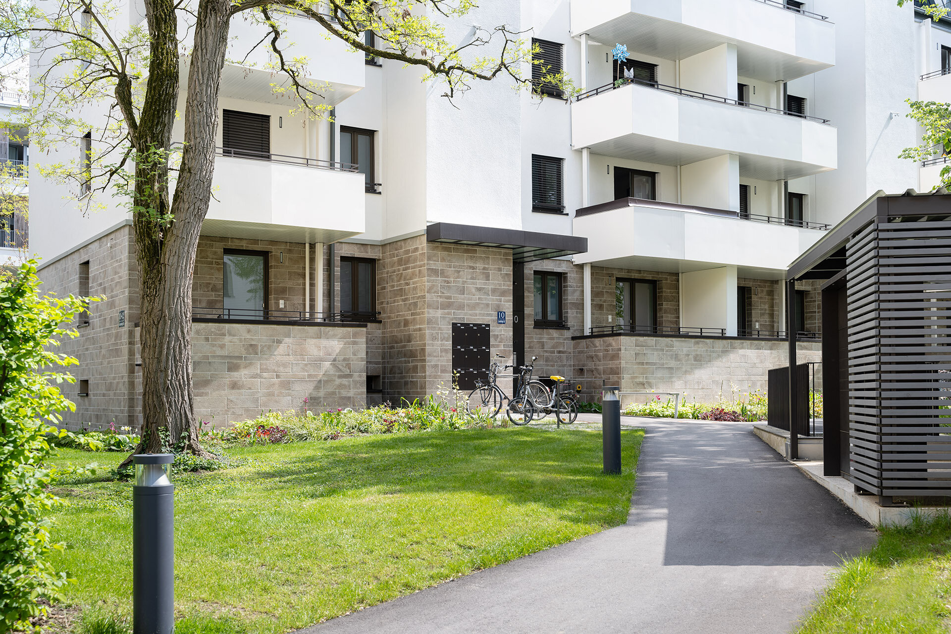 Fußgängerweg zum Neubauobjekt mit Fahrradabstellmöglichkeit direkt vor dem Haus. Blick auf Erdgeschosswohnungen und erste Etage mit Balkonen.