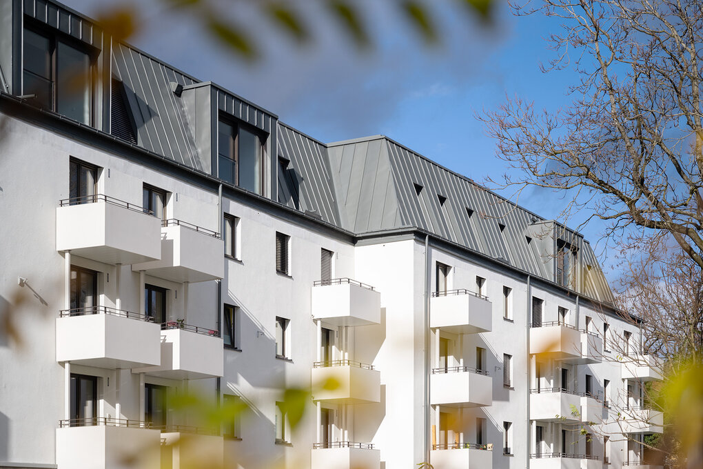 Blick auf Neubau mit weißer Fassade und geräumigen Balkonen, sowie Dachgeschossetage mit modernen Gauben