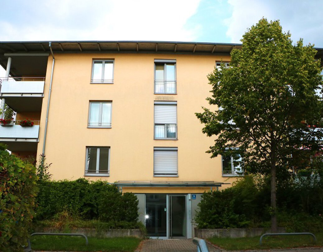 Eingang zum Wohngebäude im Philippine-Schick-Allee/Josephine-Lang-Weg. Modernes dreistöckiges Wohngebäude mit gelber Fassade und Eckbalkonen