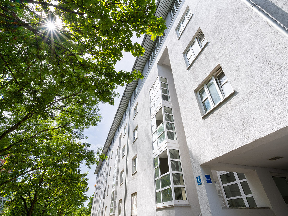 Straßenansicht des Wohngebäudes mit Hauseingang und Laubbäumen an der Straße