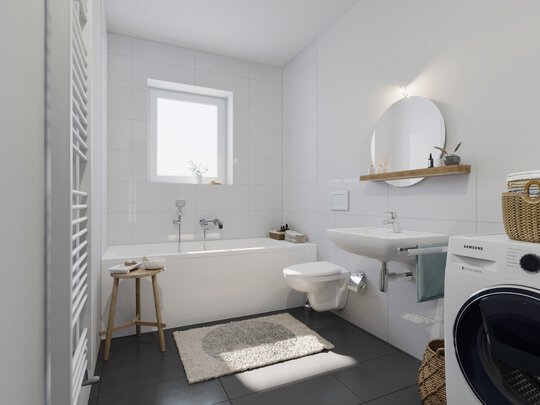 Ein weiß gefliestes Badezimmer mit einer Badewanne auf der linken Seite. Ein Holzschemel steht neben der Badewanne. Gegenüber der Badewanne befindet sich ein weißes Waschbecken mit einem runden Spiegel darüber. Darunter steht eine Waschmaschine. Der Boden ist dunkel gefliest.