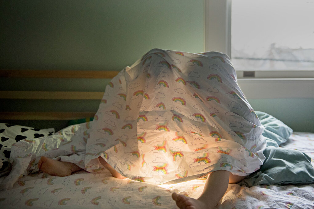 Zwei Kinder unter einer Bettdecke mit warmem Licht – ein Moment der Geborgenheit im eigenen Zuhause.